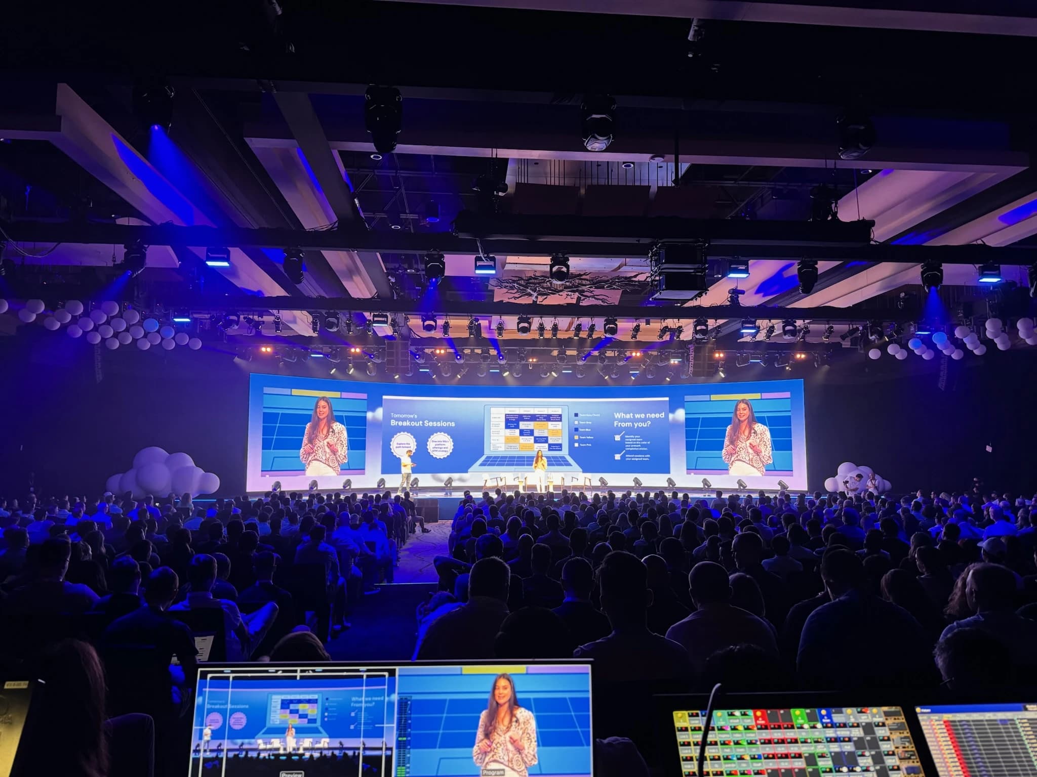 A keynote stage with a curved LED backdrop in front of a large conference audience