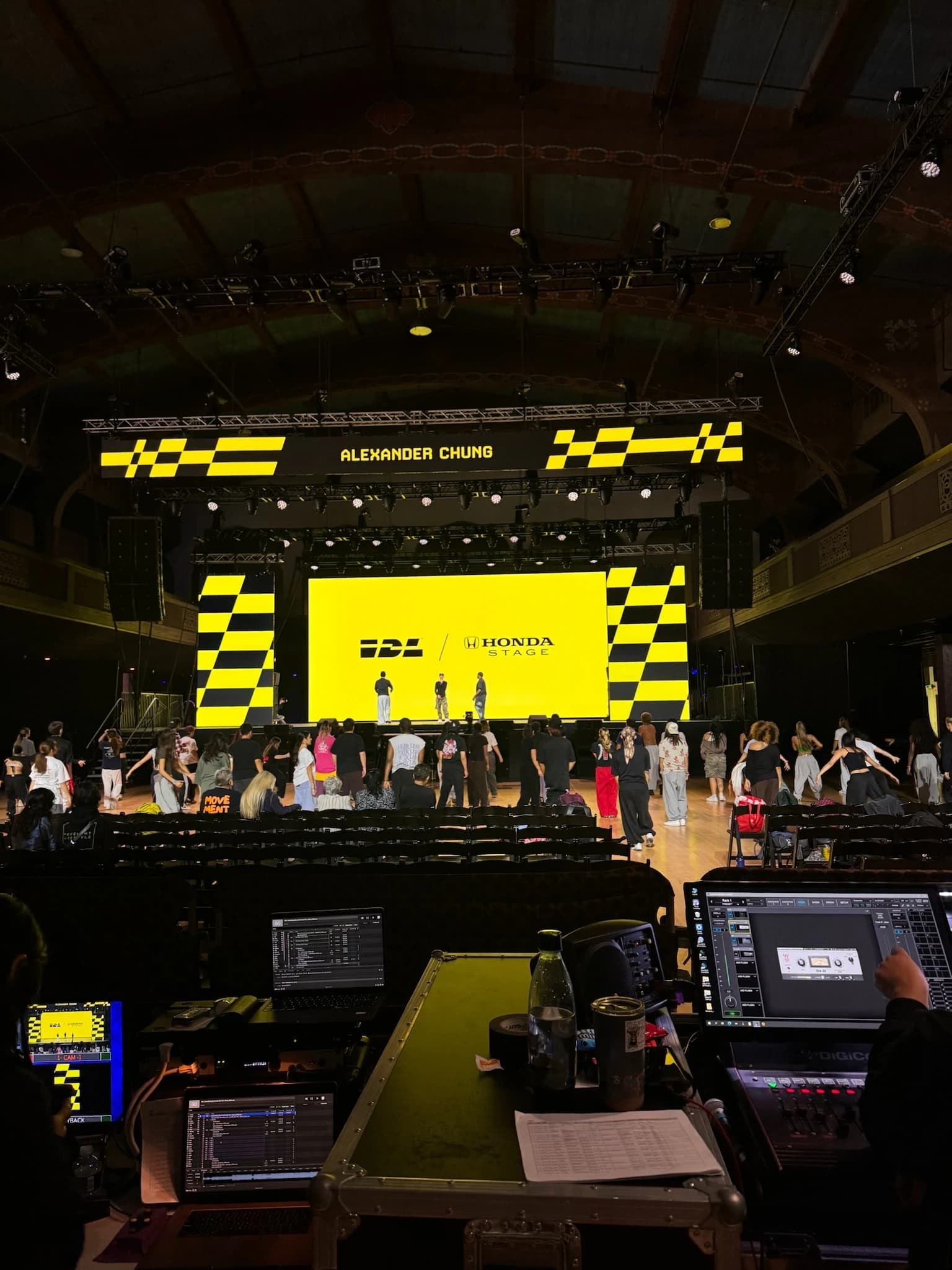 International Dance League on the Honda Stage — a checkered yellow-and-black LED wall and header truss in a historic auditorium, seen from the front-of-house console position during rehearsal.