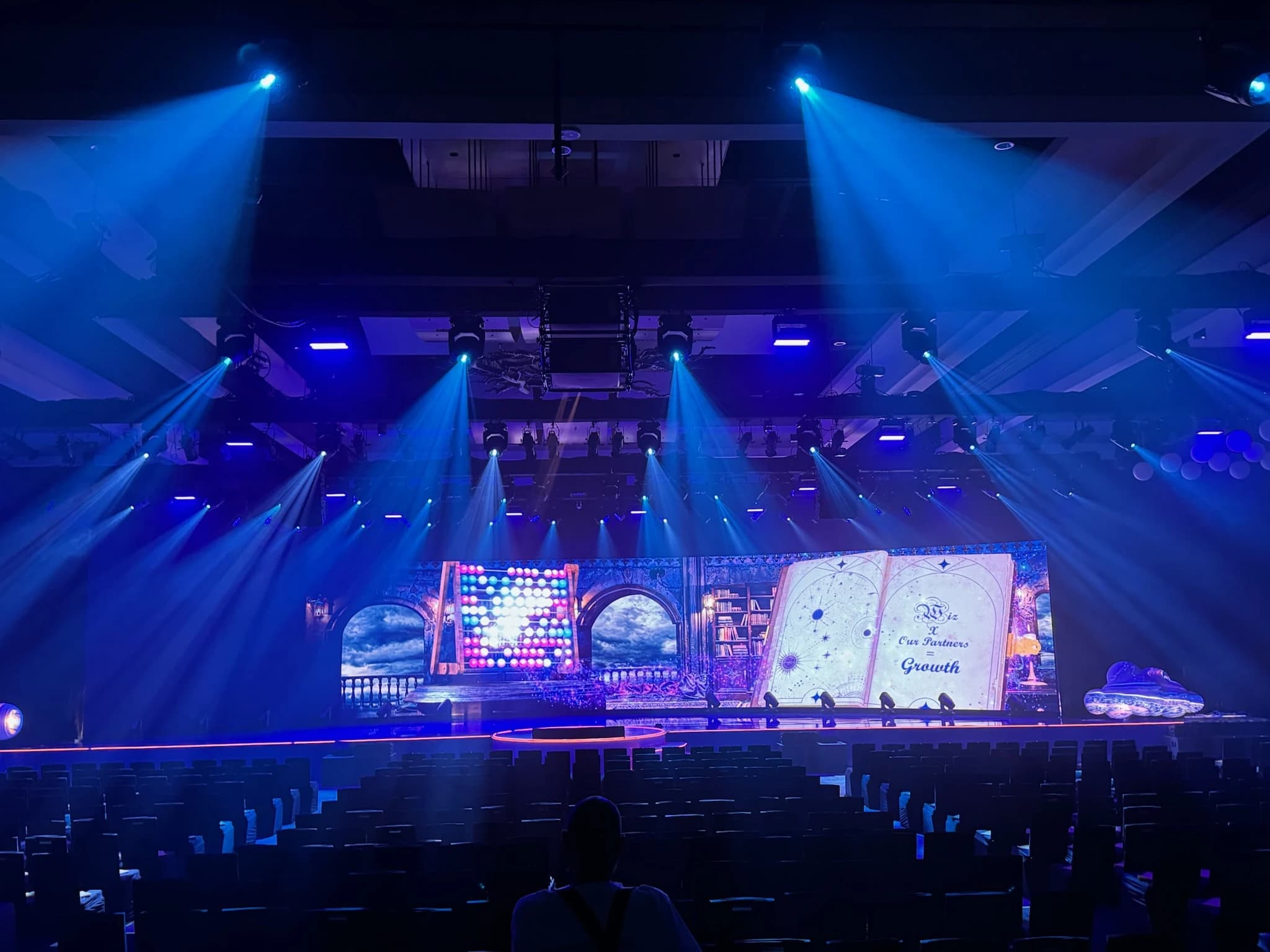 Corporate general session in a ballroom before doors — a wide LED wall carrying a themed partner graphic, a blue beam rig overhead and banquet seating set.