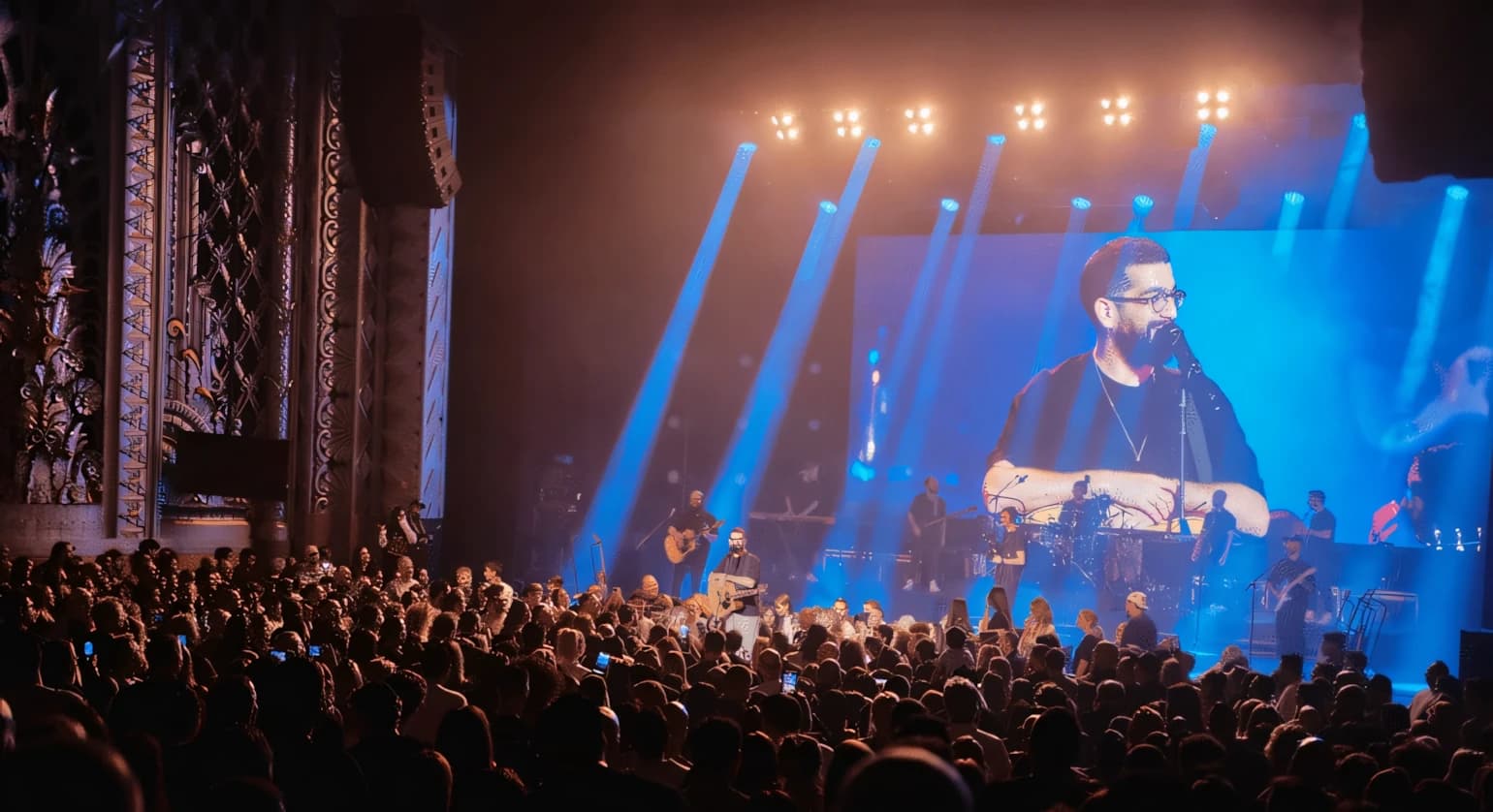 A concert stage lit with blue beams from moving lights on overhead truss